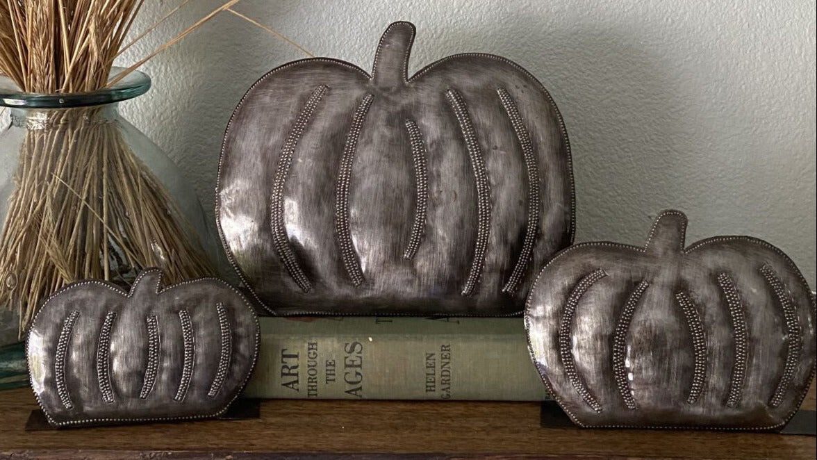 Decorative metallic pumpkins on a shelf with books and a decorative vase.