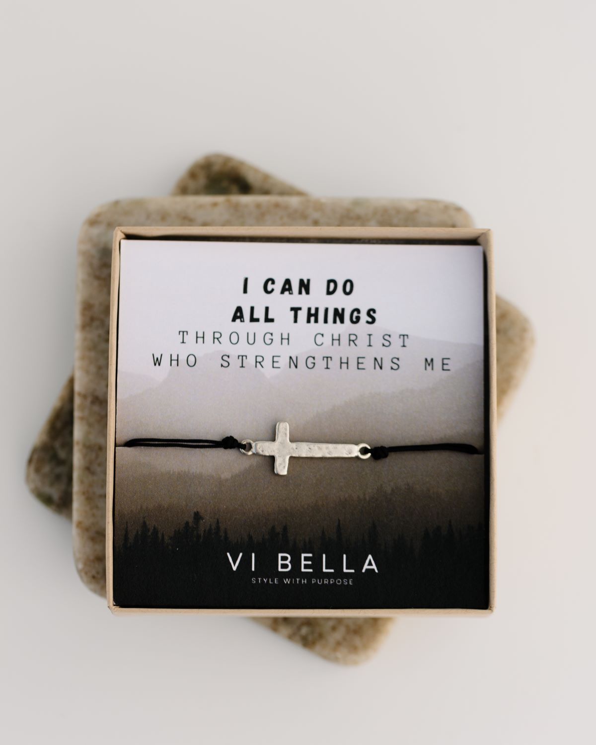 A silver-plated textured cross on an adjustable black cord bracelet, presented in a box with a scripture verse.