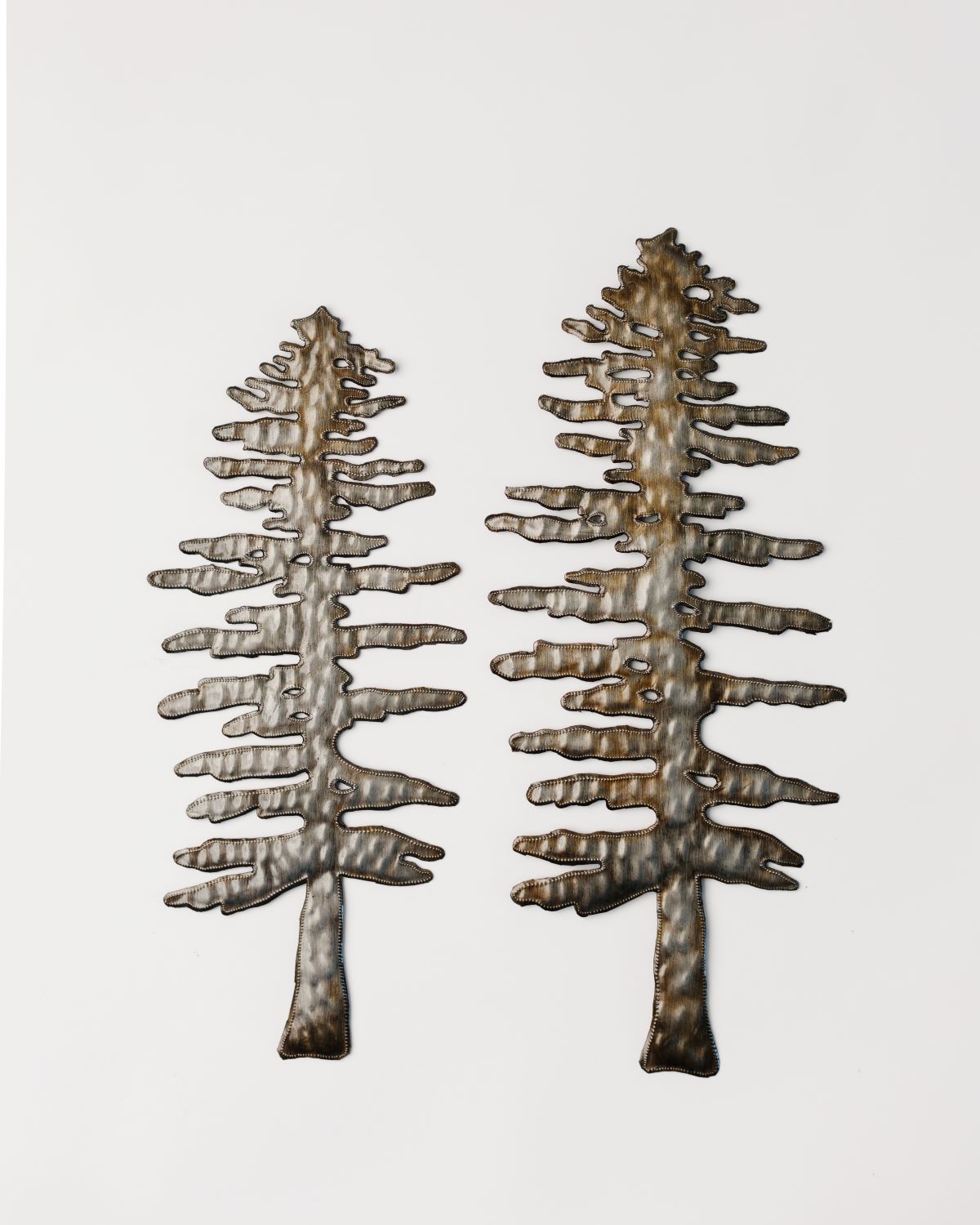 A set of two metal art sculptures of pine trees with a rustic finish, handcrafted and displayed against a white background.