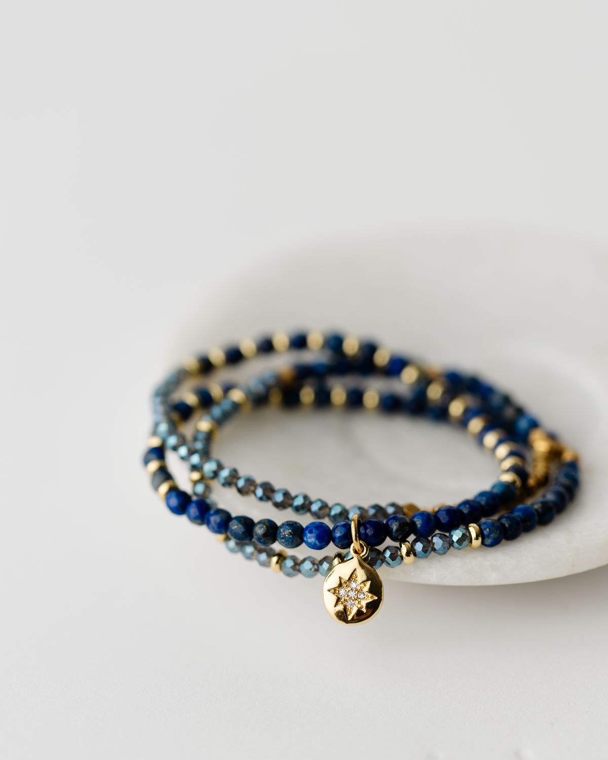 20" stretch cord to be worn as a necklace or wrap bracelet, featuring gold and blue beads and a gold north star pendant