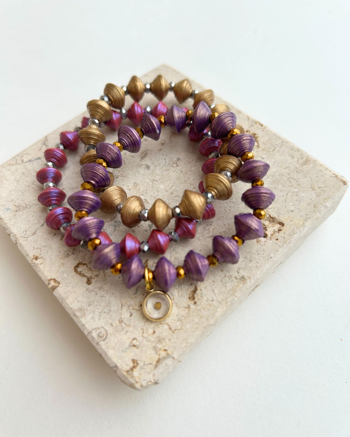 Stack of purple and gold beaded bracelets on a stone surface