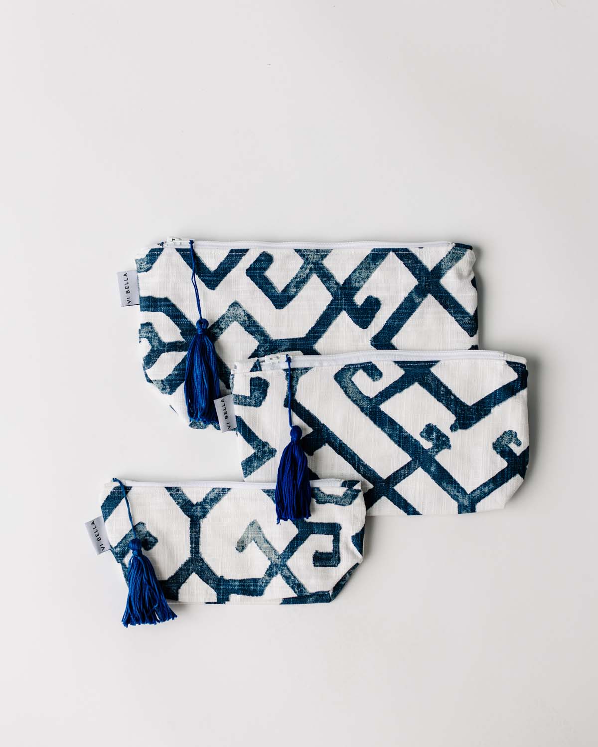 A set of three matching cosmetic bags with geometric blue and white patterns and handmade tassels.