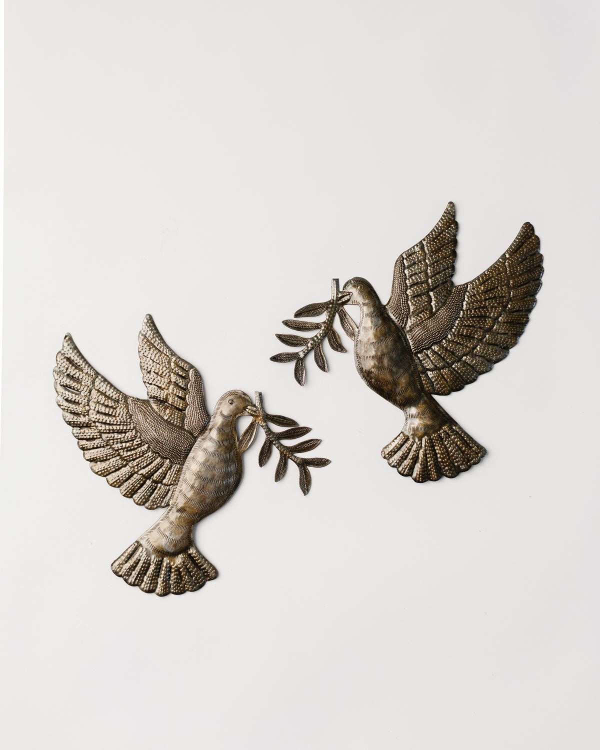 A set of two metal doves with an olive branch, handcrafted from recycled materials, with a hammer and chisel.