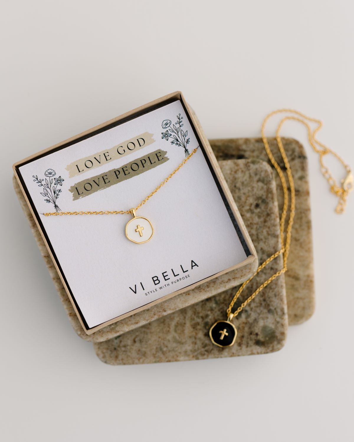 Emily Necklace displayed in a branded box with a card that reads 'LOVE GOD LOVE PEOPLE', featuring a gold-plated brass chain with a gold cross pendant, available in ivory or black enamel.