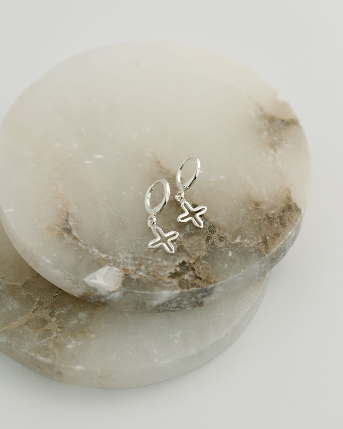 Silver cross earrings on a marble stone