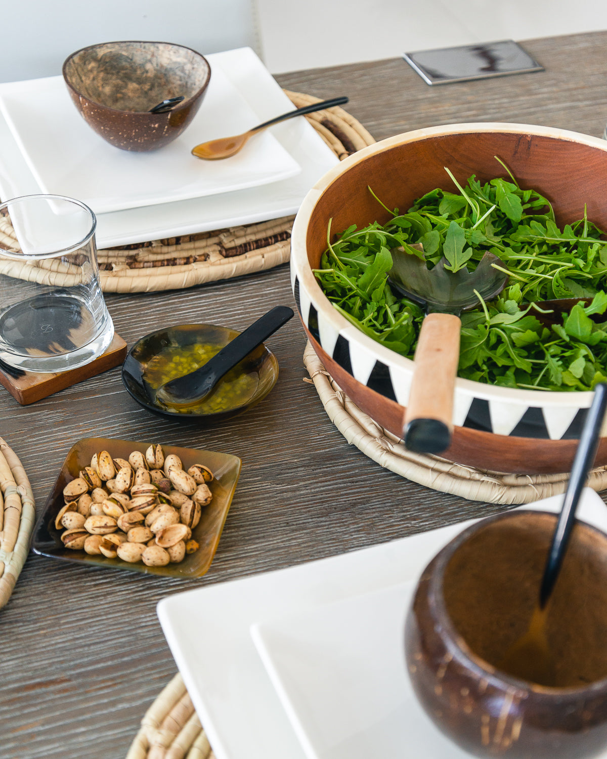 A horn dish on a dining table alongside a salad bowl and a glass of water, with the dish carved from ethically sourced horn.