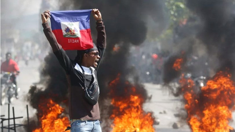 Man holding up Haitian flag in front of burning tires
