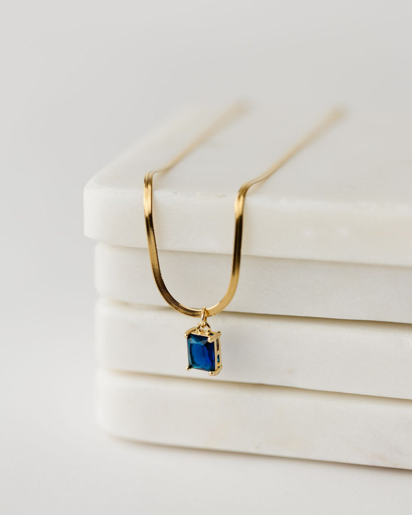 Dark blue cubic zirconia rectangular pendant in 24k gold setting on a 17.5" gold plated herringbone chain