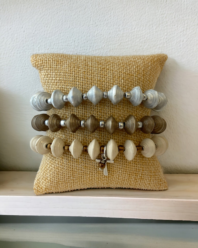 Set of 3 paper bead bracelets with a silver cross charm displayed on a bracelet pillow.