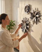 Woman arranging decorative floral wall art on a light-colored wall.