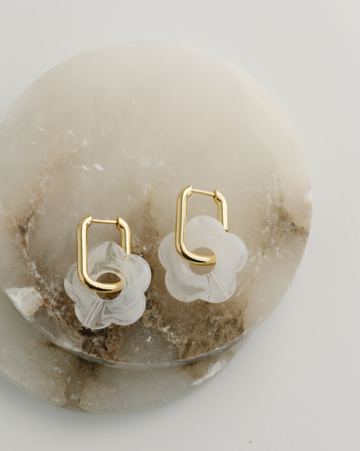Gold hoop earrings with white floral designs on a stone surface