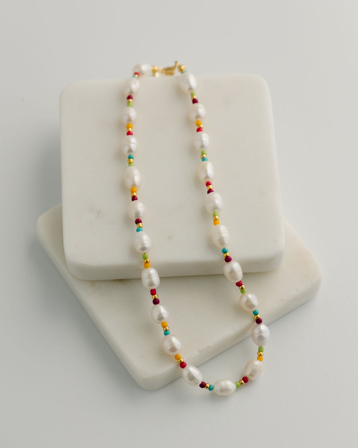 Necklace with pearls and colorful accents on a white stand against a light gray background