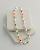 Necklace with pearls and colorful accents on a white stand against a light gray background