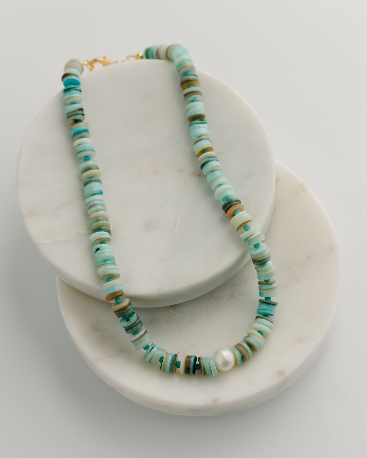 Necklace with turquoise and gold beads on a white marble stand