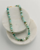 Necklace with turquoise and gold beads on a white marble stand