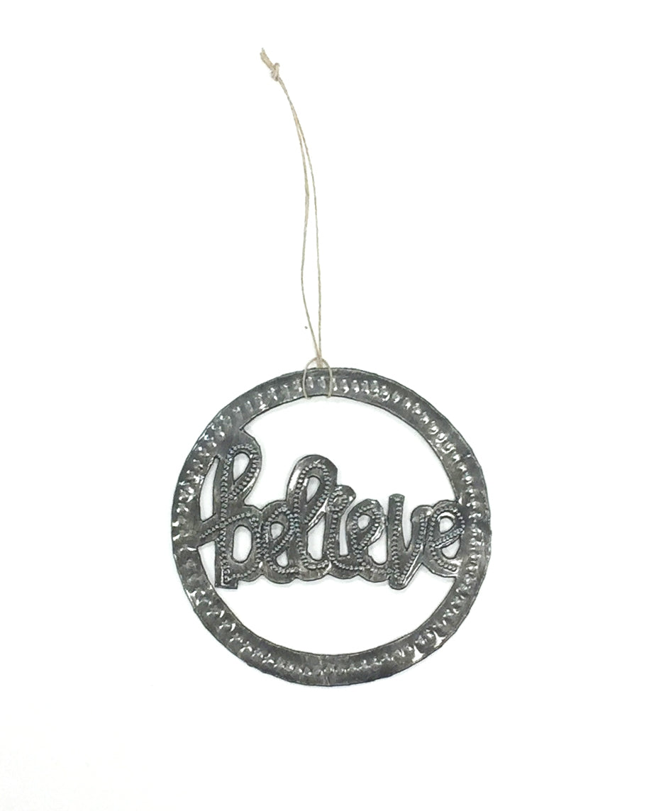 A metal art ornament with the word 'BELIEVE' inscribed in a circular pattern, with a hanging ribbon at the top.